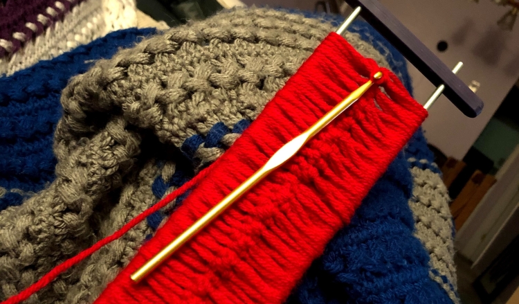 A golden crochet hook attached to red yarn and a hairpin lace crochet apparatus