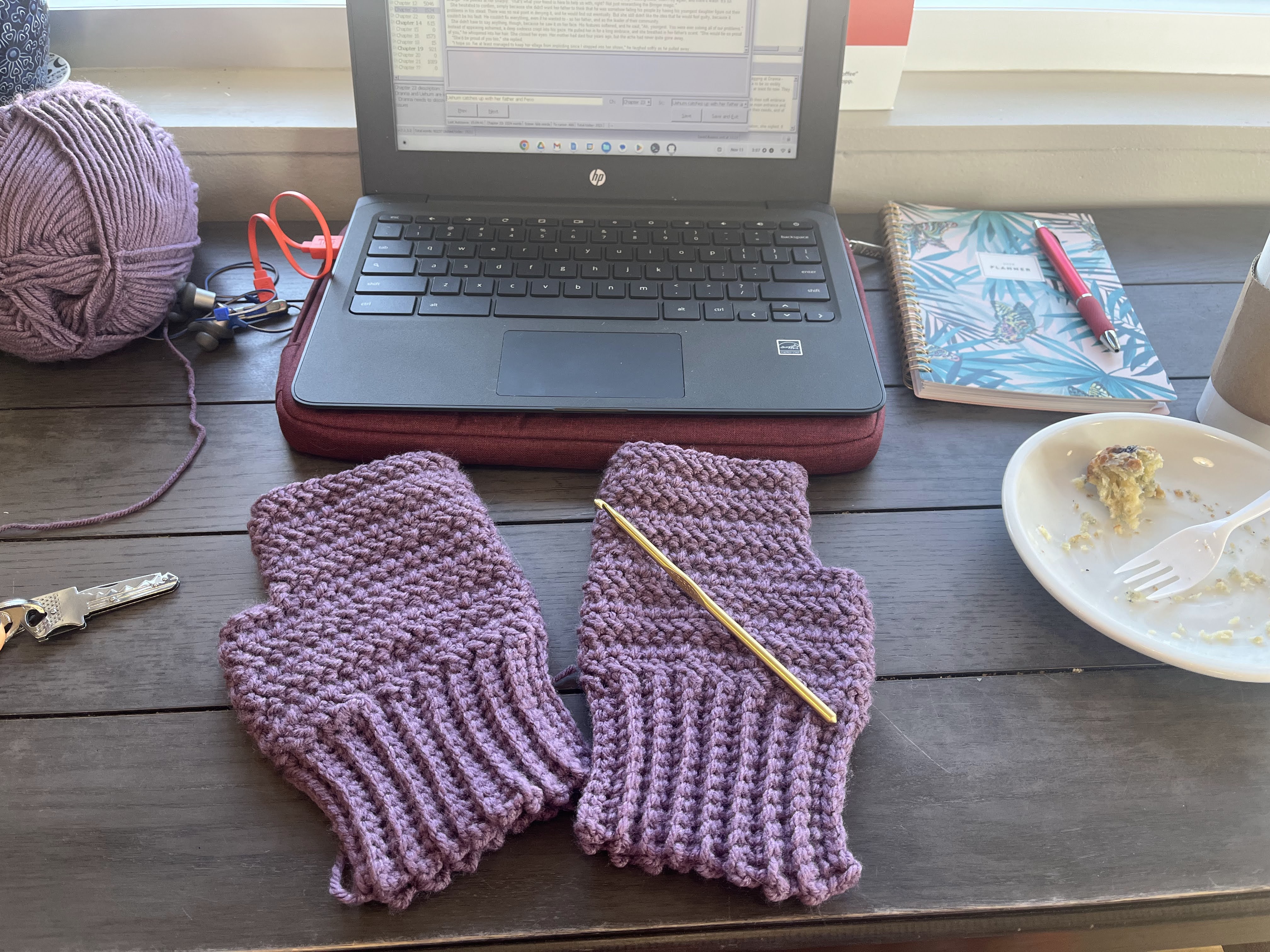 A pair of crochet gloves in front of a laptop